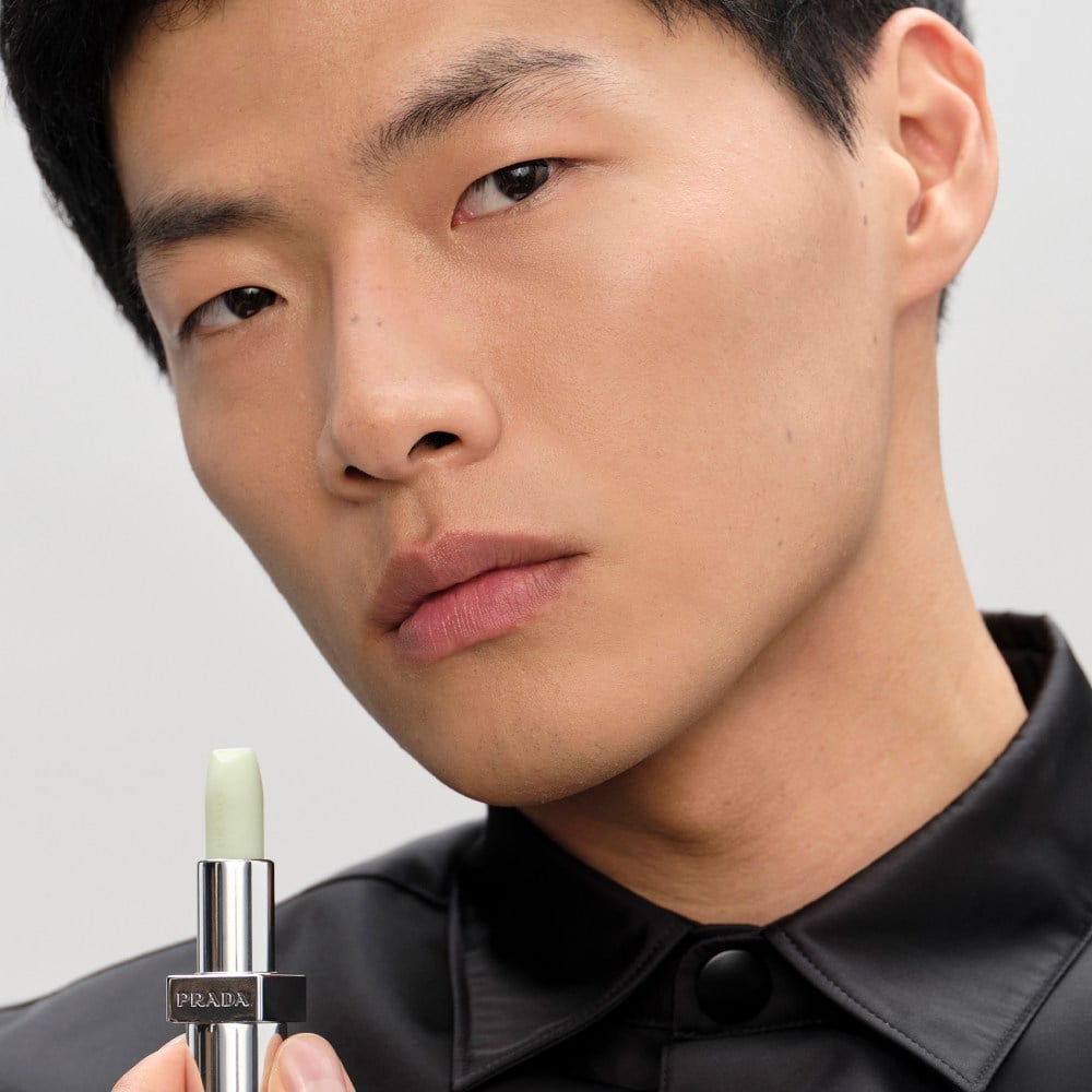 Chris (Asian Male Model) is wearing Prada Balm in shade Universal with product in hand on a neutral background 