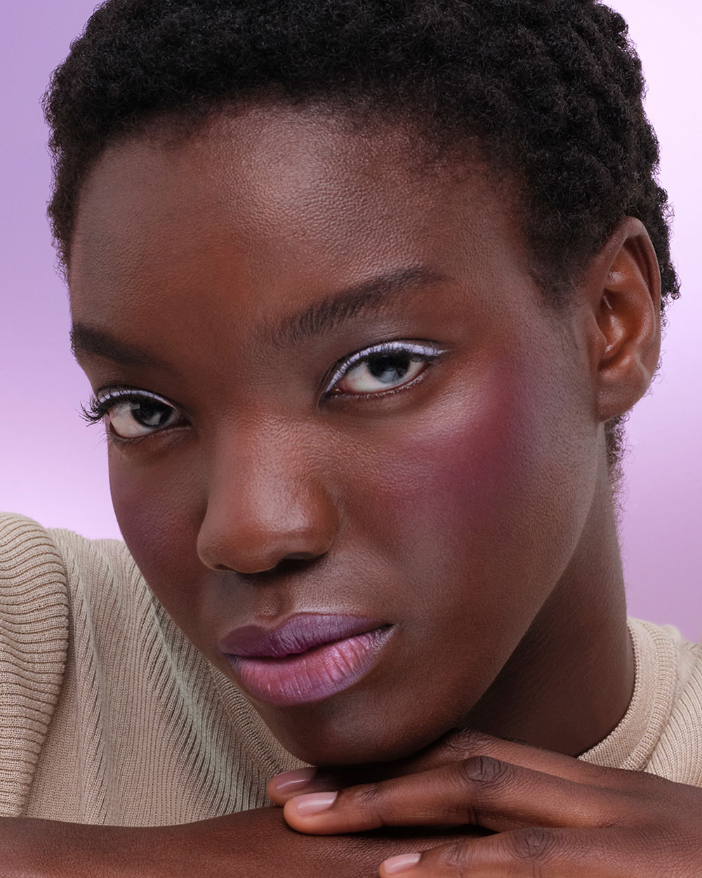 Ama (Deep Skin Model) is wearing Prada Lines Eye Pencil in shade 06 Glycine and Pradascope Mascara in shade 01 Nero on a purple background.