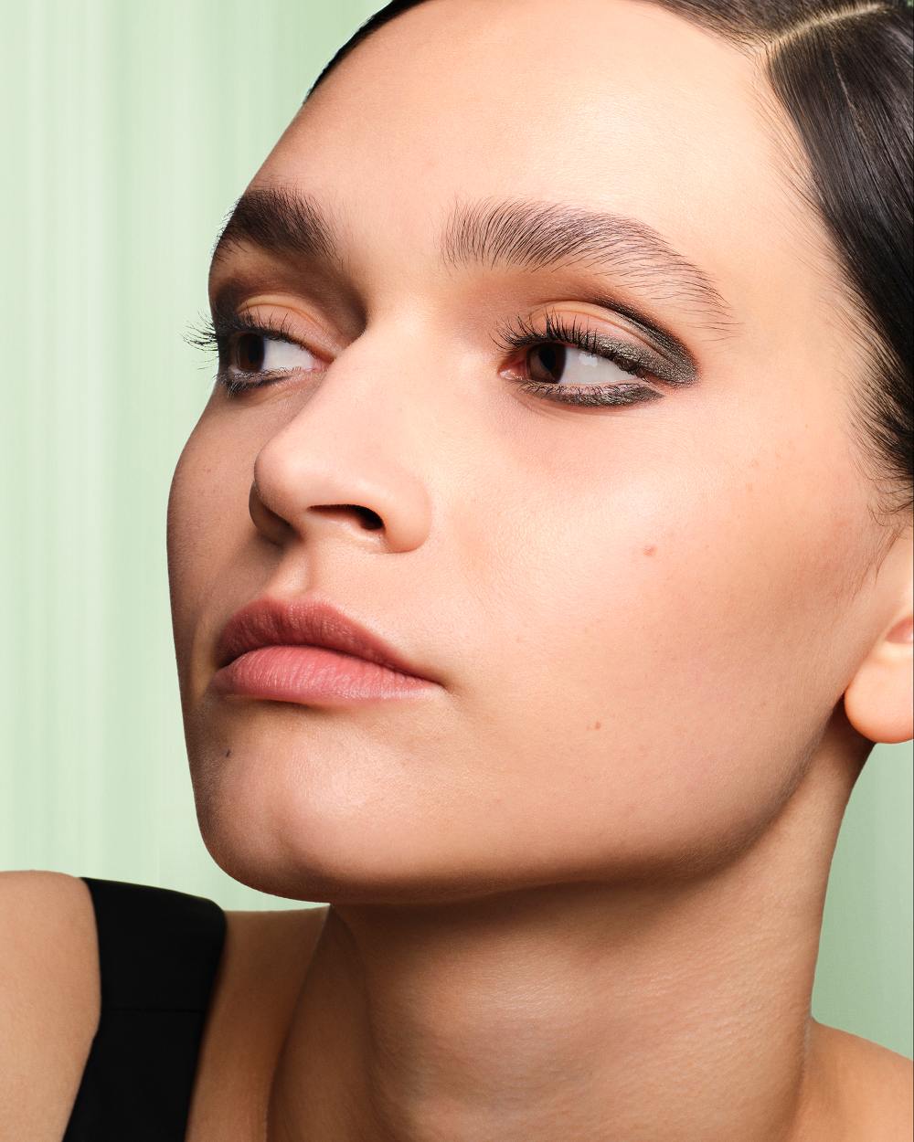 Alina (Light Skin Model) is wearing Prada Lines Eye Pencil in shade 04 Ember on a light green background. 
